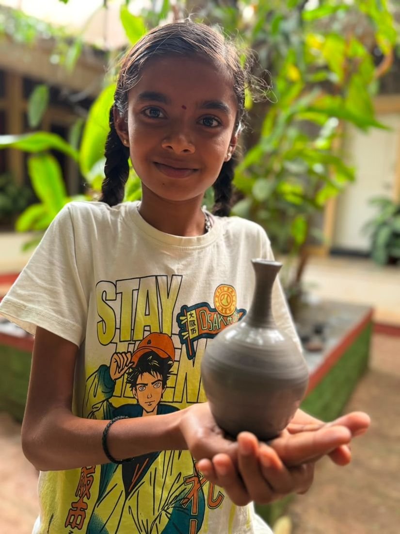A smiling girl holding the clay vase she made