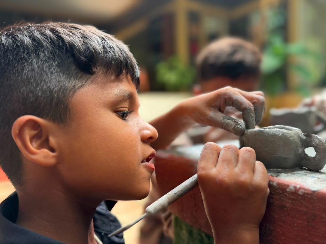 A young boy sculpting a clay figure with a modelling tool