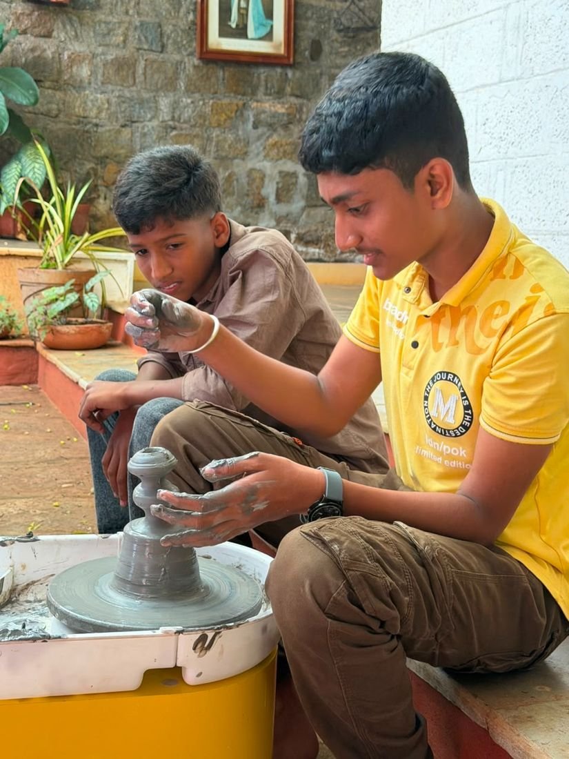 A teenager throwing a pot on the wheel as a younger boy looks on