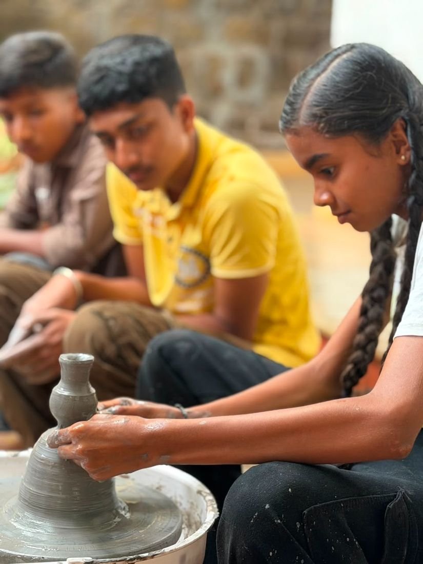 A student shaping a vase on the potter's wheel while others watch