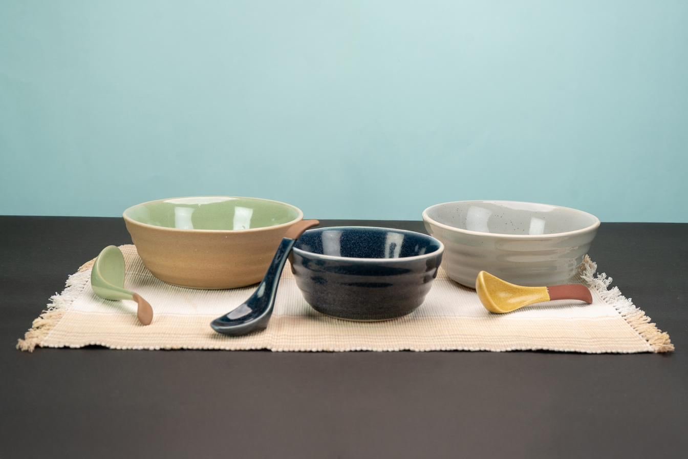 Bowls in sage, charcoal and grey with ceramic spoons on a woven runner