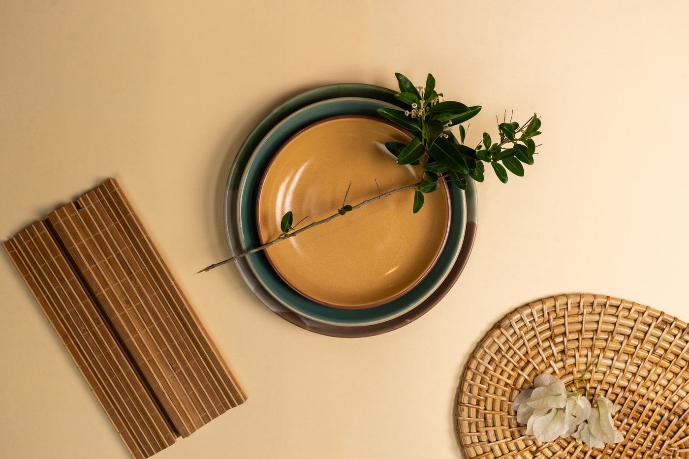 A mustard bowl nested in teal and grey plates with a leafy sprig